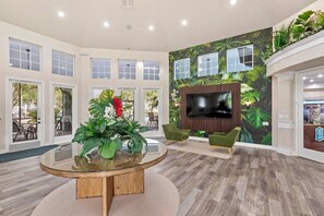 A spacious lobby with a round glass table, green chairs, a large TV, and a tropical mural. - Valentina’s Condo-Resort Style! (Kissimmee)