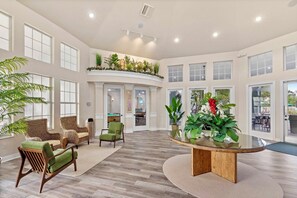 A spacious interior with a high ceiling, large windows, and a central round table surrounded by chairs. - Valentina’s Condo-Resort Style! (Kissimmee)
