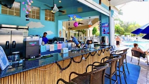 Un área de bar al aire libre con mostrador, asientos y una piscina al fondo.