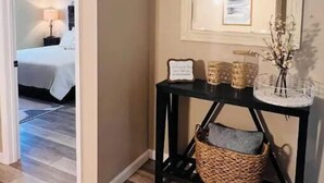 Un pasillo con una cama al fondo, una consola decorada con objetos y un espejo en la pared.