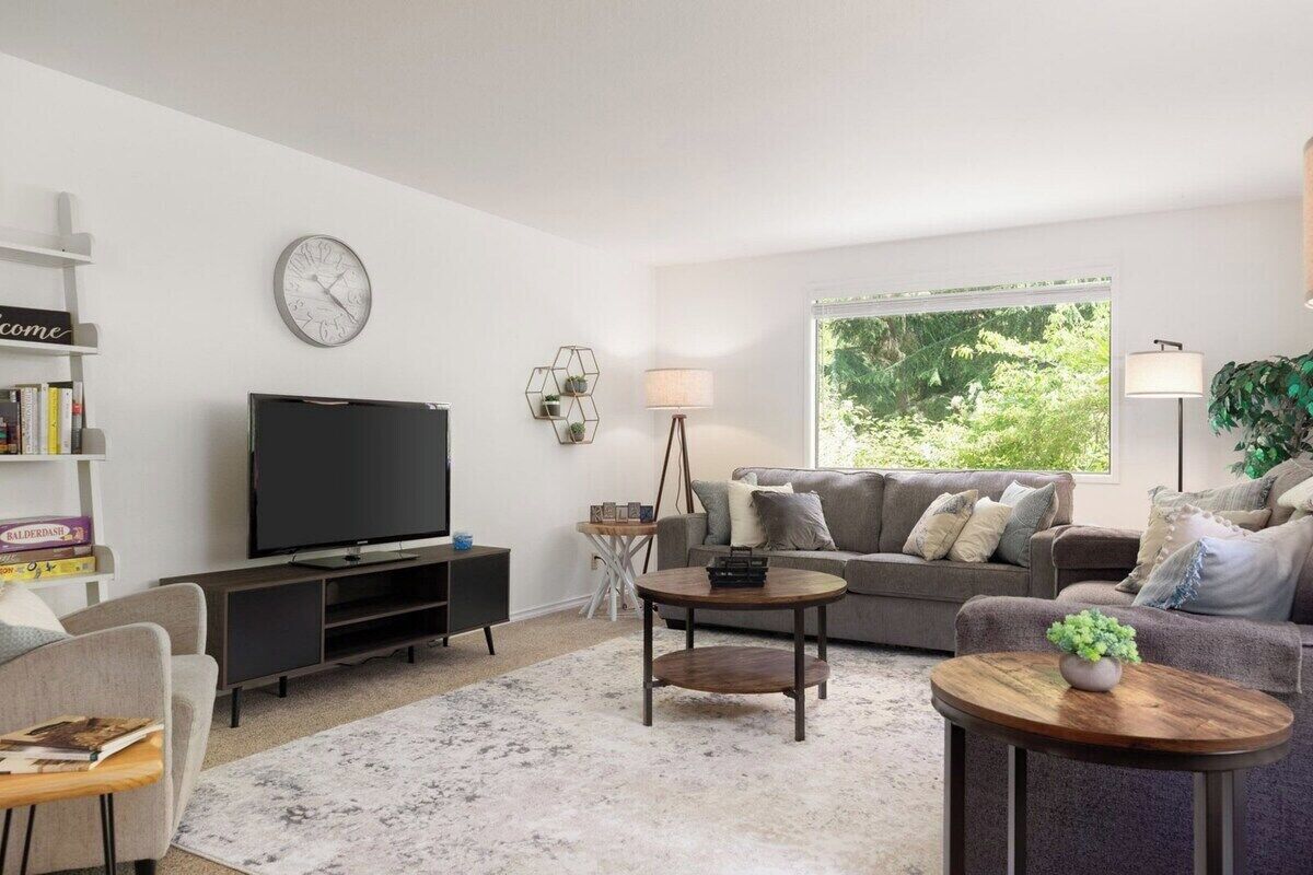 Ett modernt vardagsrum med en platt-TV, en grå soffa, ett soffbord och en bokhylla.