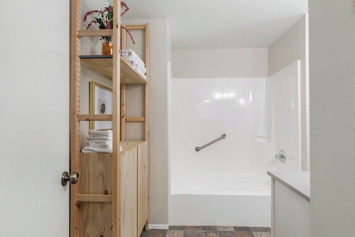 Un baño con una bañera blanca, zona de ducha y un armario de madera con toallas.
