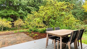 A wooden deck with a table and chairs, surrounded by lush greenery and trees. - Perch - Island Hideaway in Historic Nature Reserve (Coupeville)