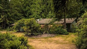 A house surrounded by dense forest, with a well-maintained lawn and various shrubs. - Perch - Island Hideaway in Historic Nature Reserve (Coupeville)