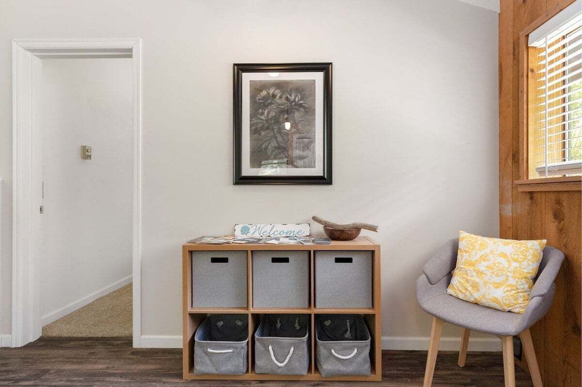 A hallway with a wooden bench, grey storage bins, a framed artwork, and a chair with a cushion.