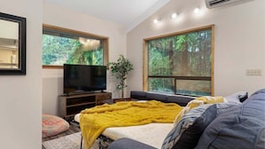 A modern bedroom with a bed, a TV, and large windows offering a forest view.