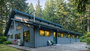 A modern cabin with a sloped roof, large windows, and a gravel driveway.