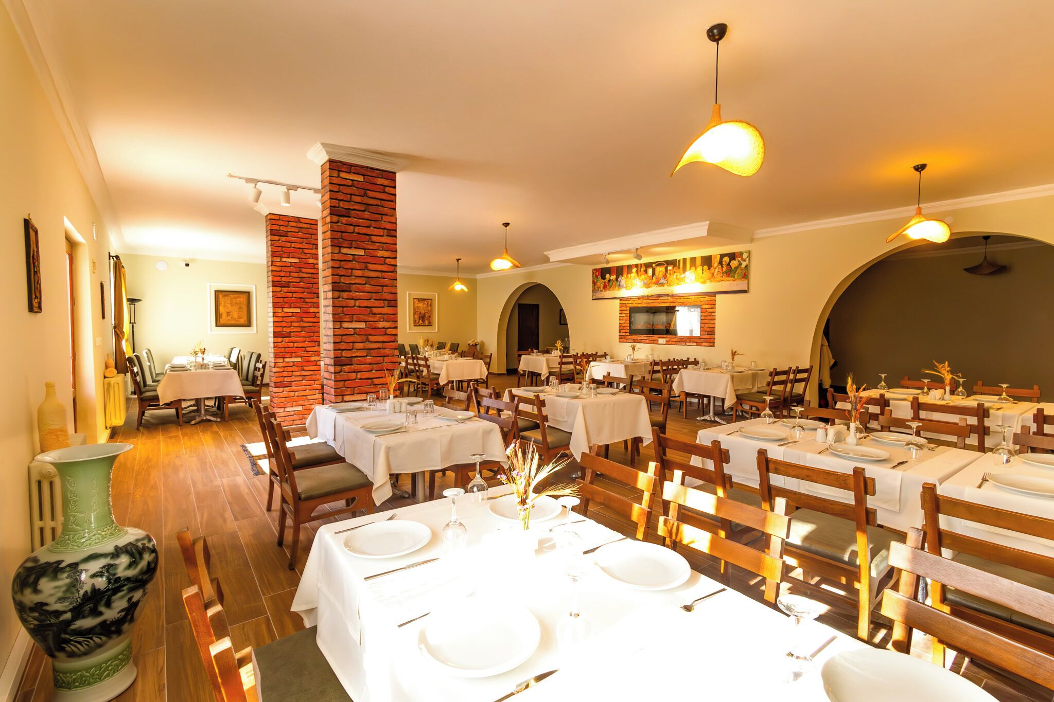 A restaurant with multiple tables set for dining, featuring a brick column and a mural on the wall.