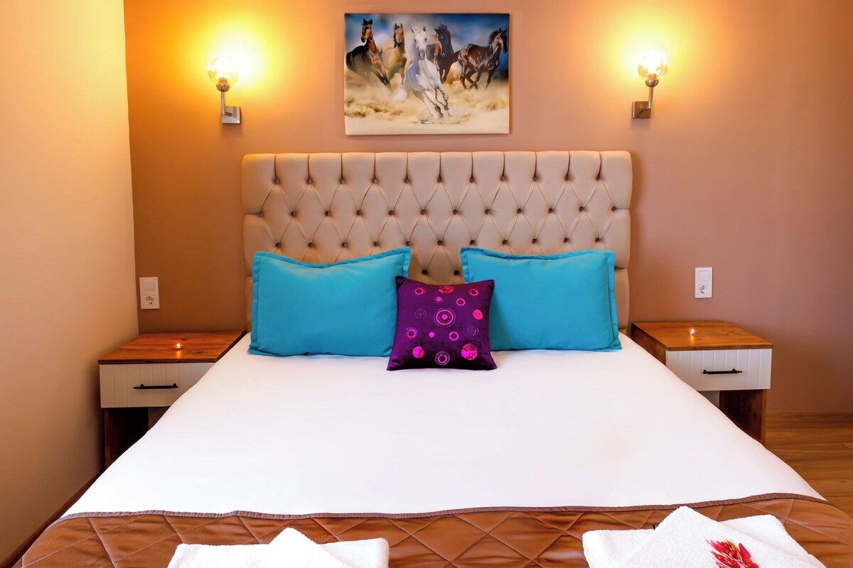 A neatly made bed with a tufted headboard, two bedside tables, and a painting above.