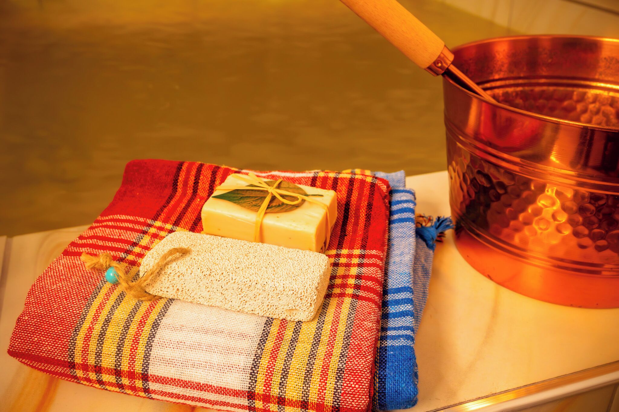 Une casserole en cuivre, un pain de savon et un morceau de tissu tissé, le tout posé sur une surface en bois.