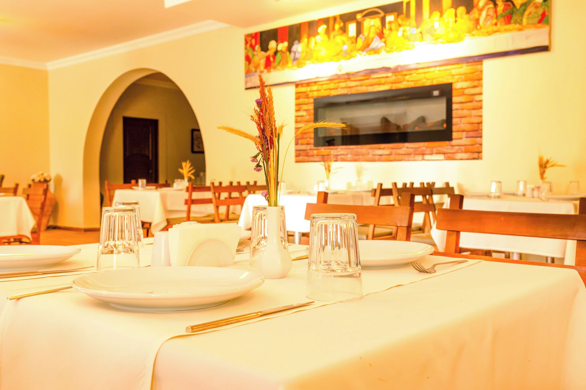 A dining area with tables set for a meal, a fireplace, and a mural on the wall.