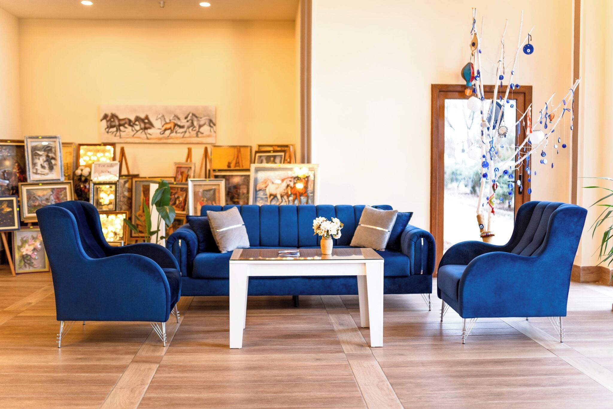 Een moderne woonkamer met een blauwe zithoek, een witte salontafel en een decoratieve boomsculptuur.