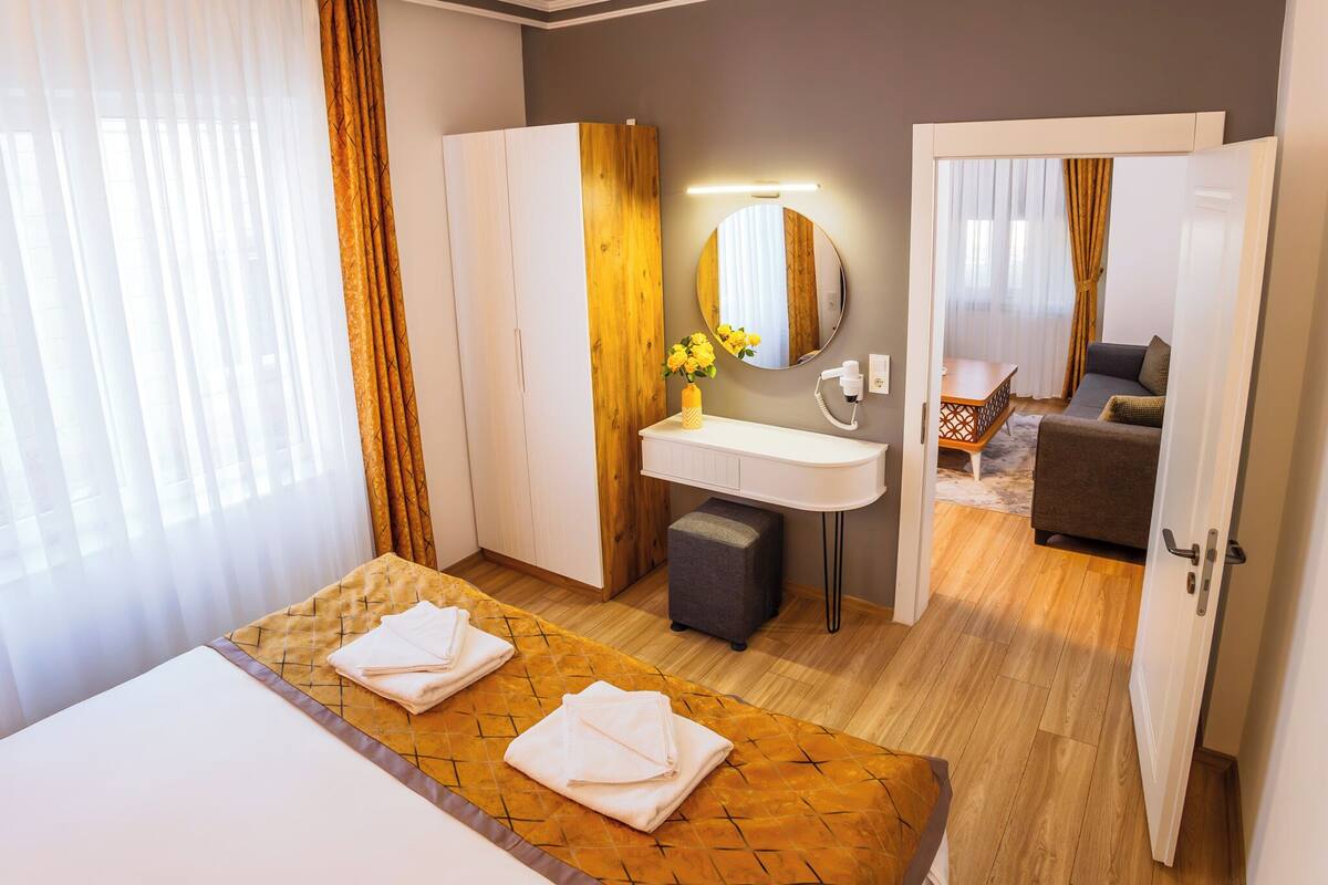 Une chambre d’hôtel avec un lit, une salle de bain dotée d’un miroir, d’un lavabo et d’une petite table sur laquelle est posé un vase de fleurs.