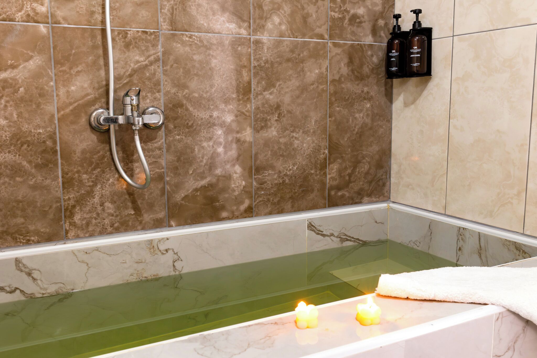 Un baño con bañera de hidromasaje con mampara de vidrio, ducha y estante con art ículos de aseo.