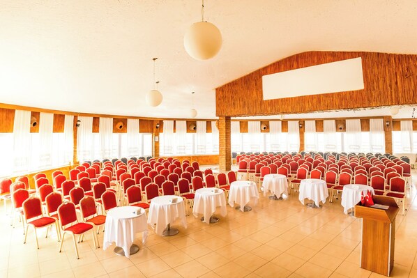 A conference room with rows of red chairs and white tables, large windows, and a wooden accent wall. - Continent Hotel Kapadokus Thermal (Guzelyurt)