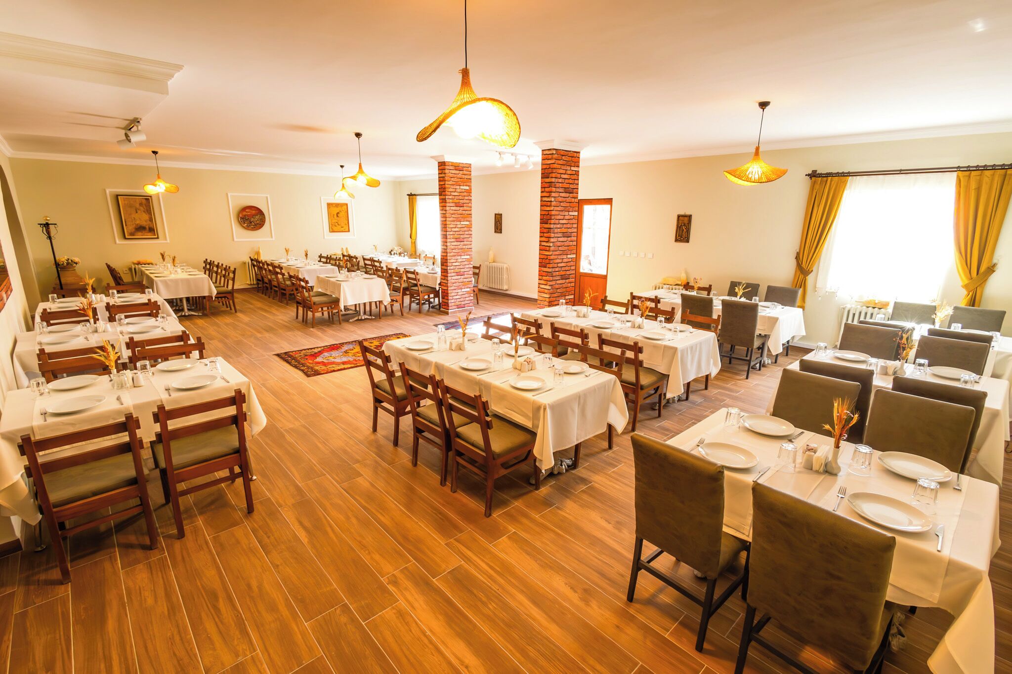 A spacious dining area with multiple tables and chairs, wooden flooring, and hanging pendant lights.