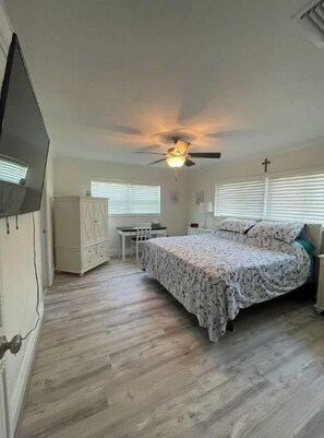 Um quarto com cama, ventilador de teto, escrivaninha e guarda-roupa.