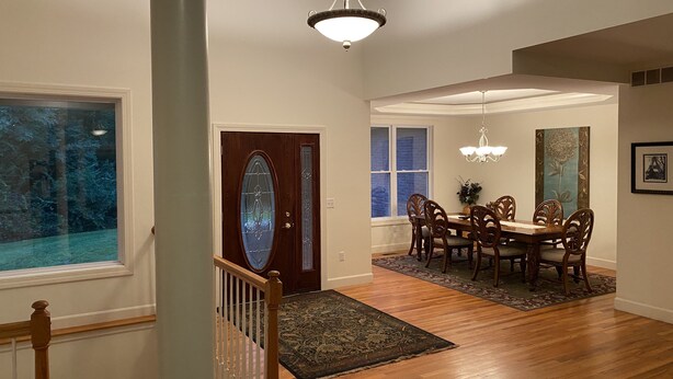 A dining area with a wooden table and chairs, a chandelier, and a large window with a view of trees. - 5-acres, Large 5-Bedroom Home with possible 6th Nursery next to Master Bedroom. (Morrow)