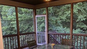 A covered outdoor area with a glass table and chairs, surrounded by wooden railings and large windows. - 5-acres, Large 5-Bedroom Home with possible 6th Nursery next to Master Bedroom. (Morrow)