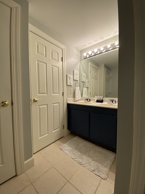 A bathroom with a white door, a vanity with a dark cabinet, a sink, and a mirror with lights.