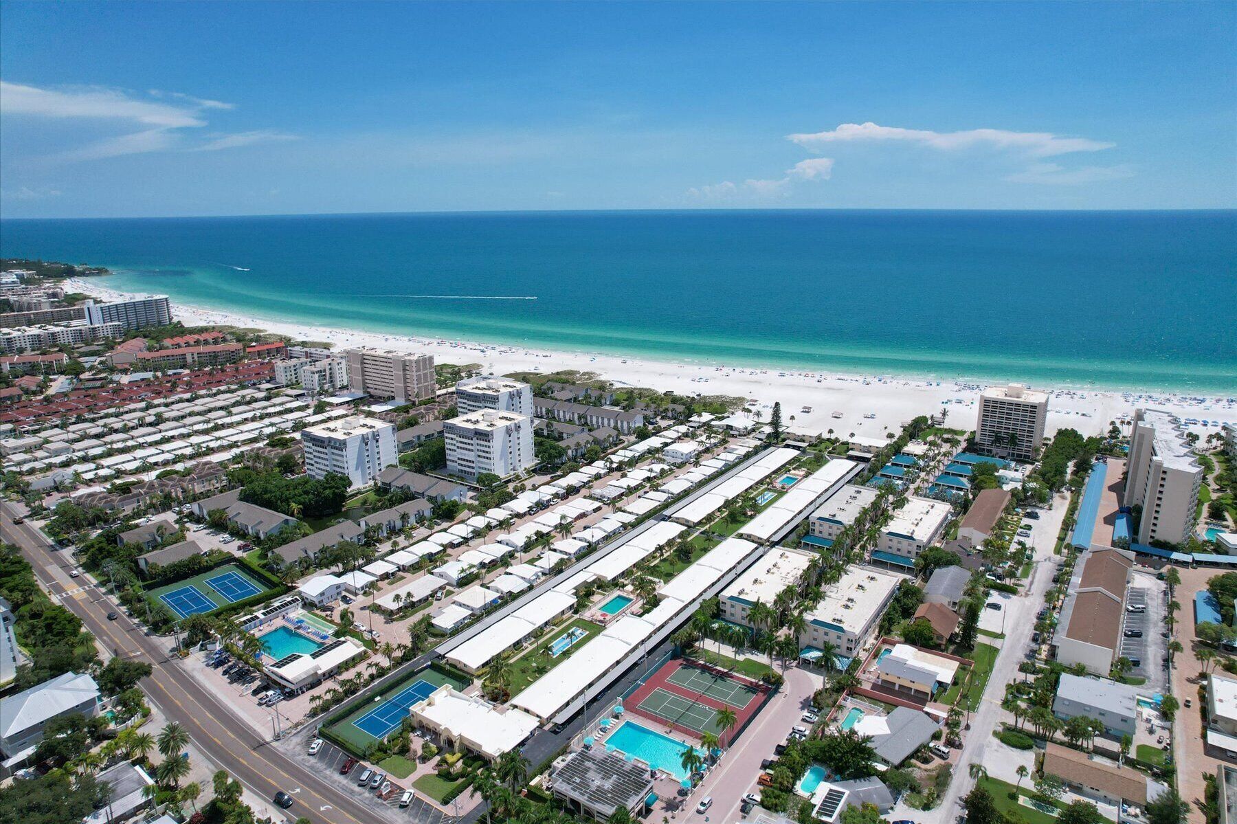An aerial view of a coastal hotel area with multiple buildings, a beach, and a clear blue sky.
