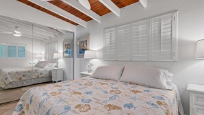 A bedroom with a large bed, a bedside table, a mirror, and a window with shutters. - Welcome to Siesta Dreams at Casa Mar!! (Siesta Key)