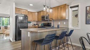 Una cocina con armarios de madera, un refrigerador de acero inoxidable, un microondas, una cafetera y una zona de bar con taburetes.