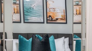 Un dormitorio con cama, cabecera, espejo y tres cuadros en la pared.