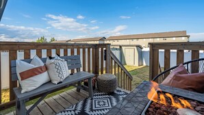 Una terraza de madera con una chimenea, asientos exteriores y vistas a edificios de apartamentos.