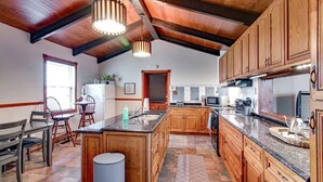 A spacious kitchen with wooden cabinets, a large island, and a high ceiling with exposed beams.