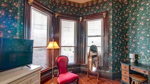 A room with a television on a dresser, a red chair, a mirror, and a vanity with drawers.