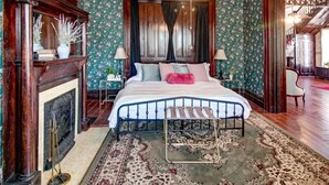 A bedroom with a bed, a fireplace, a ceiling fan, and floral wallpaper.