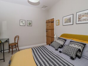 A bedroom with a bed, a wooden wardrobe, a desk, and framed pictures on the wall. - 5 East Street (Skipton)