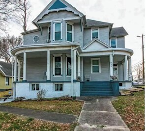 Una casa de dos pisos con un porche que rodea toda la casa y una puerta azul.