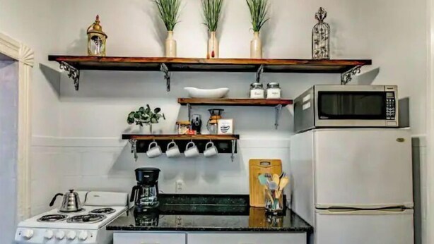 A kitchen with white cabinets, a stove, a microwave, and a coffee maker. There are potted plants on a shelf above the stove. - ❤DT Victorian Apt D❤ 1br~Walk to DT/APSU~Firepit❤ (Clarksville)