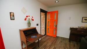A hallway with a wooden desk, a vase with flowers, and a bright orange door. - The Ranch Near Boomer Lake (Stillwater)