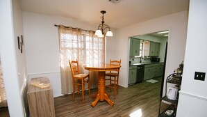 A dining area with a wooden table and chairs, a chandelier, and a view into the kitchen. - The Ranch Near Boomer Lake (Stillwater)