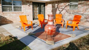 A patio with four orange chairs, a large red vase, and a brick house with a door and windows. - The Ranch Near Boomer Lake (Stillwater)