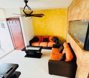 Una sala de estar con un sofá, una mesa de centro, un televisor y un ventilador de techo.
