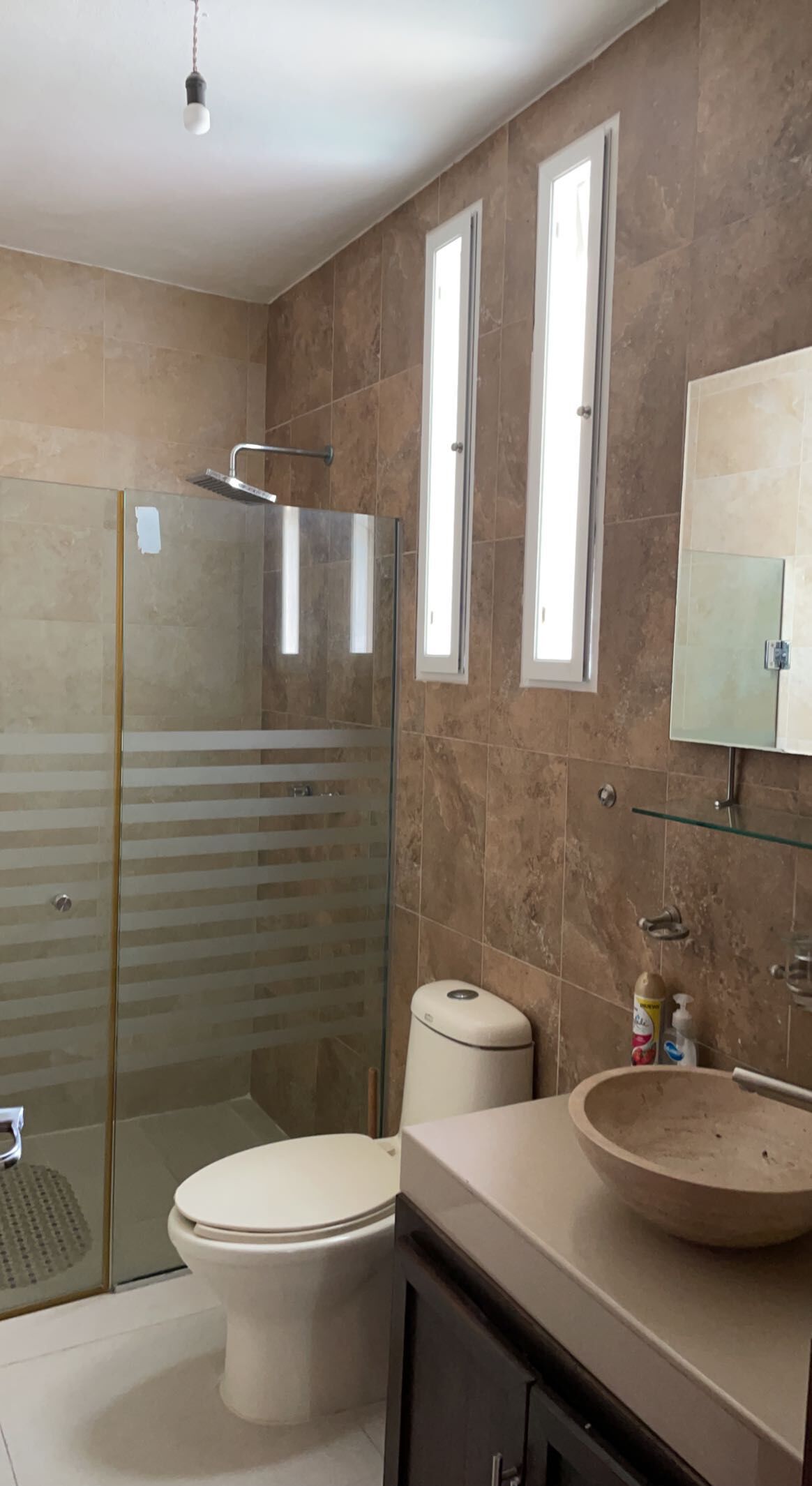 A bathroom with a glass shower enclosure, a toilet, a sink with a mirror, and a small trash bin.