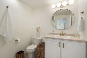 A modern bathroom with a toilet, sink, and mirror. - Whale's Tale - Boutique Studio Condo w/Pool 🐳 (Hampton)