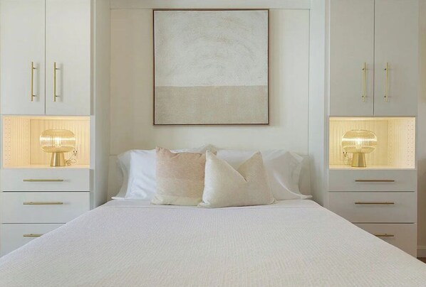A bedroom with a bed, two bedside tables with lamps, and a large framed artwork on the wall. - Whale's Tale - Boutique Studio Condo w/Pool 🐳 (Hampton)