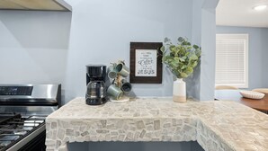 Una cocina con encimera de piedra, cafetera, una cita enmarcada y una planta en maceta.