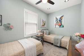 A bedroom with two beds, a ceiling fan, a window with blinds, and wall art. - DTWN KCK - 6 beds with Pool Table & Arcade Games - 7 min to PNL! (Kansas City)