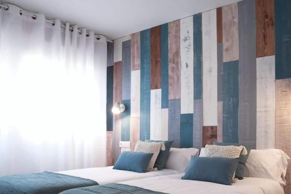 A double room with two beds, a wooden wall panel design, and a window with curtains.