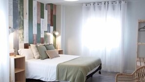 Une chambre à coucher comprenant un lit, des tables de chevet, un luminaire suspendu, une chaise et une fenêtre avec des rideaux.