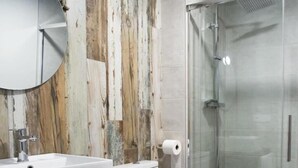 Une salle de bain moderne avec un mur arrière en bois, un lavabo blanc, des toilettes et une cabine de douche en verre.