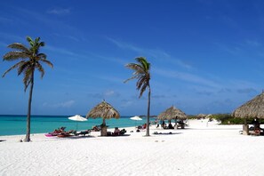 Una playa con arena blanca, palmeras y sombrillas de techo de paja.