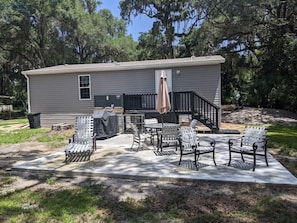 A mobile home with a patio area featuring outdoor furniture, a covered grill, and a staircase leading to a deck.