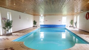 Una piscina interior con suelo de baldosas y techo de madera.